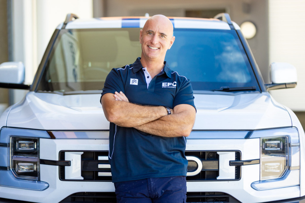 Epoxy Flooring Co team owner Tim McGary with arms crossed in front of the work vehicle