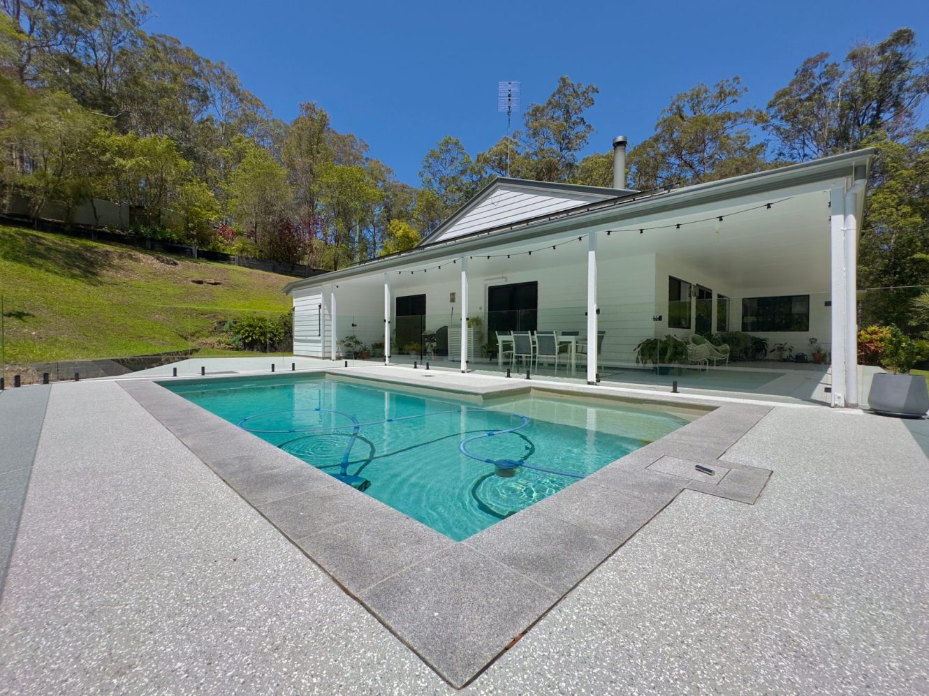Light epoxy flake pool surround with granite coping in front of a weatherboard home